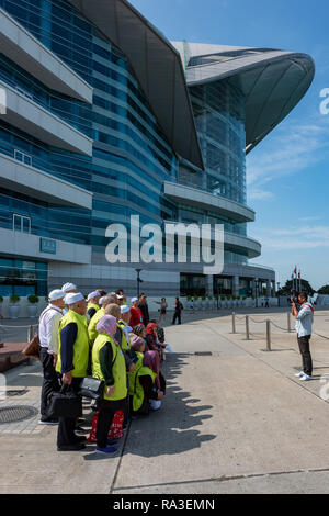 Eine der vielen täglichen Mainland China Tour Parteien vor dem Hong Kong Convention Centre in Golden Bauhinia Square posiert. Stockfoto