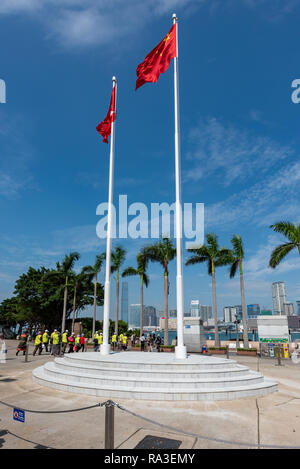 Die Hong Kong und Chinesischen Fahnen wehen über Golden Bauhinia Square mit, im Hintergrund, eine chinesische Reisegruppe tragen Hi-viz Jacken. Stockfoto