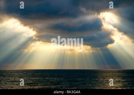 Viele lange Strahlen des Sonnenlichts durch dramatische Wolken casting lange Lichtstrahlen auf das Meer, das Meer glitzern leuchtend, Stockfoto