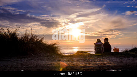 Ein paar sitzen am Rande der Sanddünen auf West Wittering Beach in der Nähe von Chichester, West Sussex. Stockfoto