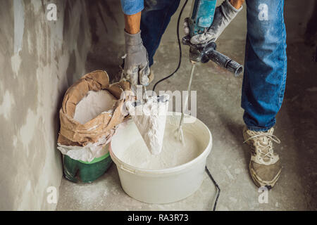 Junge männliche Maler knetet putty mit Wasser in einem Eimer mit einem Handmixer für Gebäude vereint Stockfoto