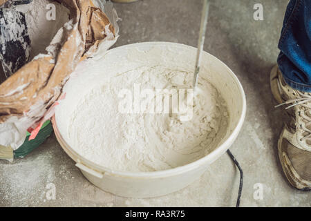 Junge männliche Maler knetet putty mit Wasser in einem Eimer mit einem Handmixer für Gebäude vereint Stockfoto