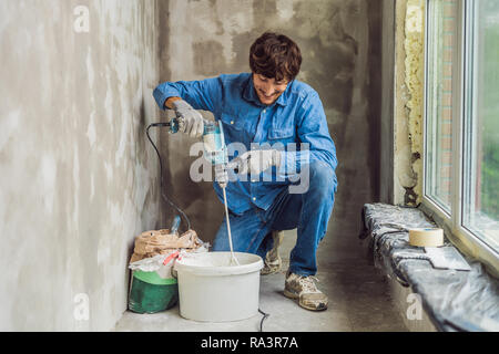 Junge männliche Maler knetet putty mit Wasser in einem Eimer mit einem Handmixer für Gebäude vereint Stockfoto