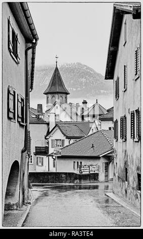 Idyllische Bergdorf in der Schweiz mit einem vlilage Straße durch alte Gebäude und viele Dächer in den Hintergrund in Schwarz und Weiß führenden Stockfoto