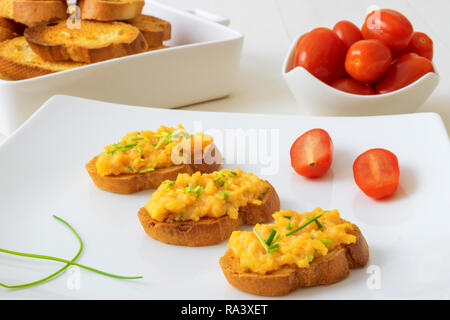 Weiße Platte mit Toast und Rührei, Schnittlauch Kräuter und Kirschtomaten auf weißem Hintergrund. Gegrilltes Brot mit Rührei und vegitable Stockfoto