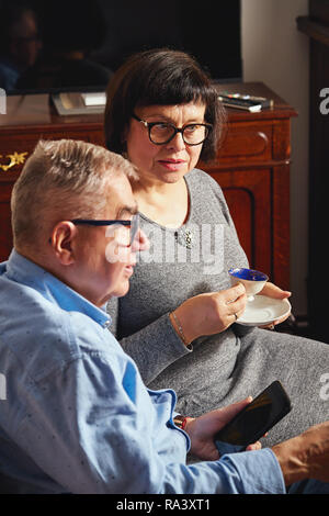 Gerne älteres Paar sitzen auf der Couch und genießen Kaffee und Tee zu Hause. Stockfoto
