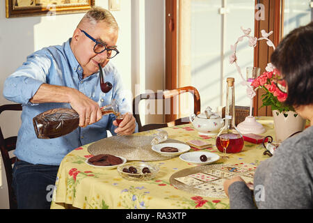 Glückliche freudige senior Paar Karten spielen und genießen eine Snacks zu Hause. Stockfoto