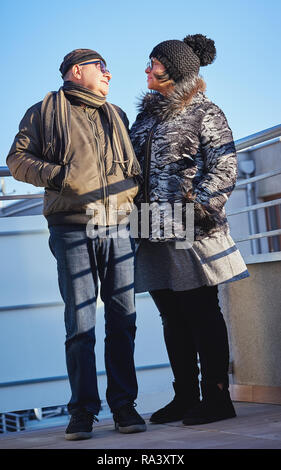 Glückliche freudige Senioren Paar warm gekleidet stehen auf dem Balkon gegen den Himmel. Stockfoto