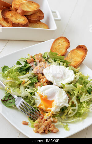 Klassische französische Salat, tolle Salat Lyonnaise. Teller mit grünen Blättern von Kopfsalat, Dijon Senf Sauce mit gebratenem Speck, gegrillte Französisches Brot, Stockfoto