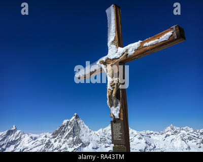 Schnee bedeckt Kreuz mit einer hölzernen Figur von Jesus Christus am Gipfel des Klein Matterhorn mit Blick aufs Matterhorn im Hintergrund, Zermatt, Schweiz Stockfoto