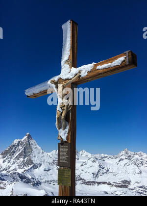 Schnee bedeckt Kreuz mit einer hölzernen Figur von Jesus Christus am Gipfel des Klein Matterhorn mit Blick aufs Matterhorn im Hintergrund, Zermatt, Schweiz Stockfoto