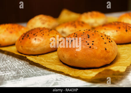 Frisch gebackene Burger Brötchen mit schwarzem Sesam auf einem backpapier. Frisch aus dem Ofen. Stockfoto