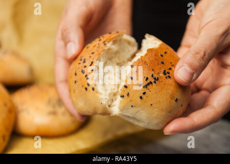 Brot in den Händen von Frau. Bäcker Hand brechen frisch gebackene Sesambrötchen Stockfoto