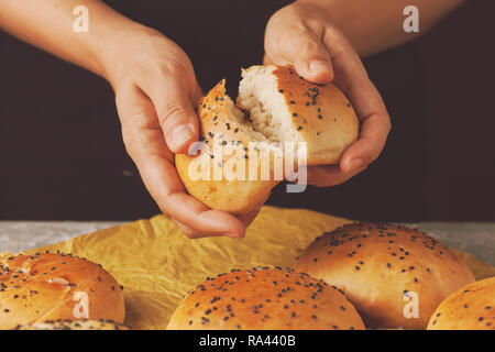 Brot in den Händen von Frau. Bäcker Hand brechen frisch gebackene Sesambrötchen Stockfoto