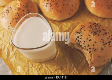 Frisch gebackene Burger Brötchen mit schwarzem Sesam auf einem backpapier. Frisch aus dem Ofen. Glas Milch Stockfoto