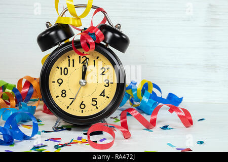 24:00 Uhr Zeit auf Retro schwarz Uhr für Silvester Party mit bunten Bändern und Konfetti auf die weiß getünchten Holz Stockfoto