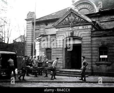 Ein Fahrzeug mit der hinteren Türen geöffnet sitzt vor einem Gebäude aus dem 19. Jahrhundert, in ein Lazarett umgewandelt wurde. (Unter dem Giebel ist eingraviert: "Turnverein Borna 1844.') Zwei Soldaten tragen eine verletzte Soldaten auf einer Bahre aus dem Fahrzeug auf die offene Tür eines Gebäudes. Stockfoto