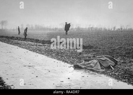 Mitte des zwanzigsten Jahrhunderts schwarz-weiß Foto mit ermordeten Opfer mit Tuch und Gendarmen und Polizisten die Inspektoren überprüfen Feld und Graben abgedeckt Stockfoto