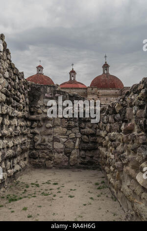 Ruinen in Mitla, mit alten Steinmauern, drei roten Stein kirchenkuppeln und ein bewölkter Himmel, in Oaxaca, Mexiko Stockfoto