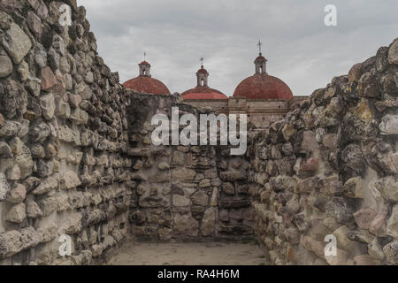 Ruinen in Mitla, mit alten Steinmauern, drei roten Stein kirchenkuppeln und ein bewölkter Himmel, in Oaxaca, Mexiko Stockfoto