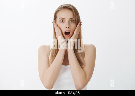 Authentische Schuß von schockiert und junges Mädchen mit blonden Haaren offenen Mund unruhigen in schüttelte und Staunen, Hände auf die Wangen und Augen wie Sehen neue Akne im Gesicht vor wichtigen Sitzung erweitern Stockfoto