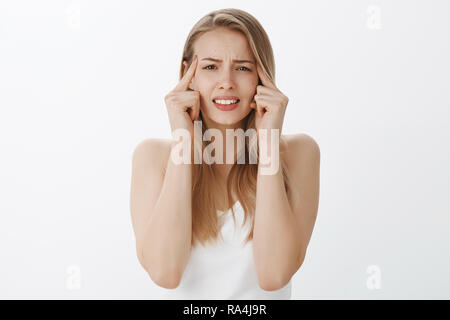 Portrait von unruhigen unbehaglich junge Schülerin unter Druck Aufeinanderpressen der Zähne und runzelte die Stirn und schielen, berühren Tempel wie der Versuch, Focus oder wichtige Sache erinnern, glitt Verstand über graue Wand Stockfoto