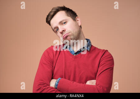 Traurige junge Mann im roten Pullover ist mit Arbeit erschöpft oder Müde des Hörens seiner Frau zu plaudern. Stockfoto