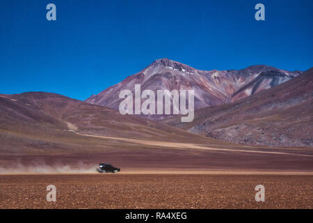 Auto fahren auf einem Feldweg in eine Wolke von Staub durch einen Berg Tal in Siloli, Bolivien Stockfoto