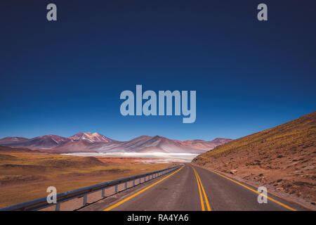 Asphaltierte Straße durch die Atacama-wüste, Chile in Richtung Berge in der Ferne und Salinen führenden Stockfoto