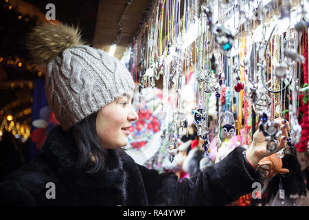 Glückliche junge Frau Wahl Weihnachten Dekoration am Markt. Modell tragen stilvolle Pelzmantel, gestrickte Mütze Hut. Outdoor Foto Stockfoto