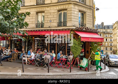 Die Menschen draußen essen Mittagessen auf dem Bürgersteig Tische im Café Bruant Restaurant und Cafe, als Street Sweeper über seine Arbeit geht, Rue des Abbesses, Paris Stockfoto