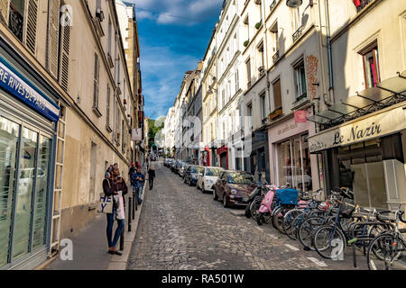 Eine Frau steht auf einer gepflasterten Straße Montmartre mit parkenden Autos, Roller und Fahrräder außerhalb Café Le Nazir, Rue Tholozé, Paris geparkt Stockfoto