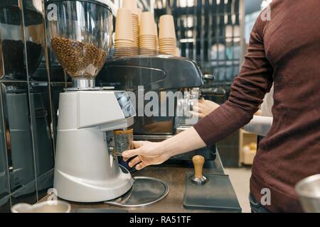 Junge barista männlichen bereitet eine Espresso Kaffeemaschine, schleifen Kaffeebohnen. Stockfoto