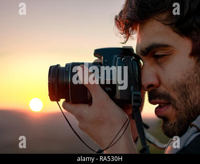 Porträt der Mann die Bilder mit der Kamera reflex gegen Sonnenuntergang. Winter Aktivitäten im Freien. Spanisch, Latein Fotografen bei Mountain Top in Spanien, 2019. Stockfoto