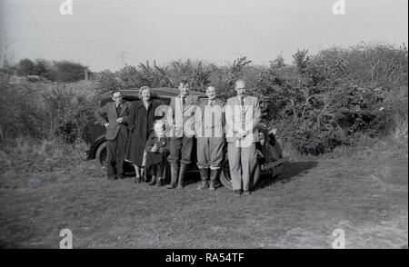 1950, historische, eine gut gekleidete Landwirtschaft Familie, mit zwei der Männer in Gummistiefeln, draußen stehen, von einem Auto, England, UK. Stockfoto