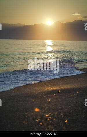 Golden Spritzer schäumenden Wellen im Meer bei Sonnenuntergang Himmel und weichen Sun hellen Hintergrund. Vertikale Farbfotografie. Stockfoto