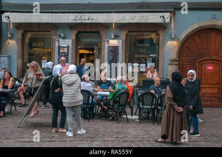 Kampf der Kulturen: weibliche muslimische Touristen beobachten westliche Touristen trinken vor einer Bar in Colmar, Elsass, Frankreich Stockfoto