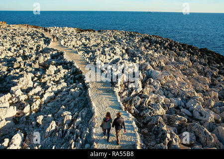 LUFTAUFNAHME von einem 6 m hohen Mast. Ein Paar, das auf einem Fußweg in einer Küstenlandschaft mit messerscharfen Kalksteinkämmen spazieren geht. Cap-Ferrat, Französische Riviera, Frankreich. Stockfoto