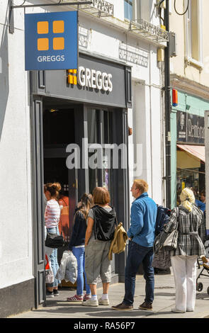 TENBY, Pembrokeshire, Wales - AUGUST 2018: Menschen außerhalb der Niederlassung der Greggs Bäckereikette in Tenby, West Wales. Stockfoto