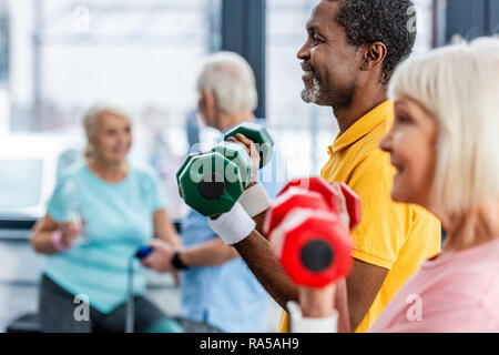 Selektiver Fokus von interracial Reifes Paar, Übung mit Hanteln im Fitnessstudio Stockfoto