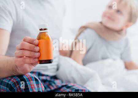 Zugeschnittenes Bild des Vaters die Pflege von kranken Sohn in Schlafzimmer und Flasche Arzneimittel Stockfoto