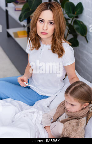 Hohe Betrachtungswinkel von Mutter die Pflege von kranken Tochter im Schlafzimmer und prüfen Sie die Temperatur mit Thermometer Stockfoto