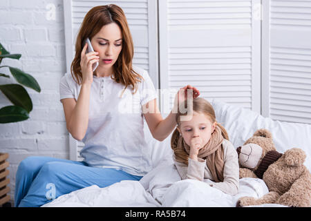 Mutter, Arzt von Smartphone und palming kranken Tochter im Bett Stockfoto