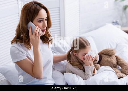 Mutter, Arzt, Smartphone, kranken Tochter blasen Nase im Bett Stockfoto
