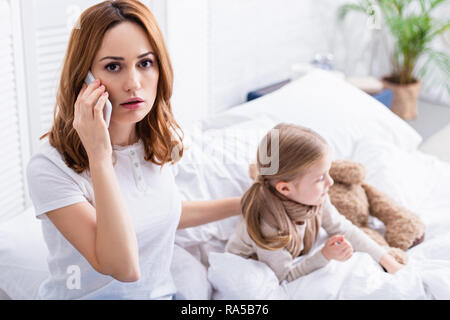 Erschrocken Mutter anrufen Arzt per Smartphone, kranken Tochter im Bett Stockfoto