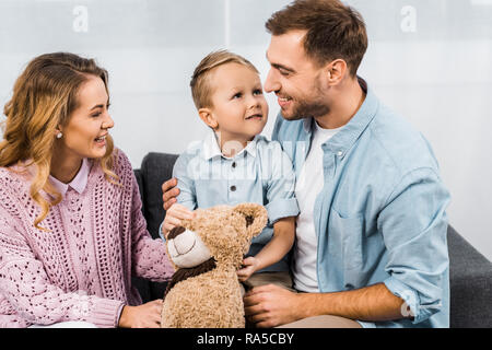 Fröhliche Eltern sitzen auf dem Sofa und die niedlichen Sohn holding Teddybär in der Wohnung Stockfoto