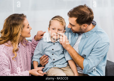 Glückliche Eltern sitzen auf dem Sofa und Berühren mit den Fingern die Nase der Sohn in der Wohnung Stockfoto