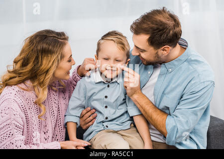 Glückliche Eltern sitzen auf dem Sofa und Berühren mit den Fingern Wangen von lächelnden Sohn in der Wohnung Stockfoto