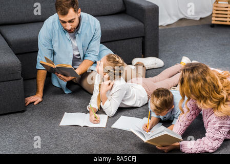 Eltern, Bücher zu lesen, während die Kinder schreiben in Notebooks auf dem Fußboden in der Wohnung Stockfoto