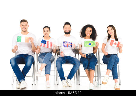 Multikulturelle Gruppe von Menschen sitzen auf Stühlen mit Fahnen der verschiedenen Länder isoliert auf weißem Stockfoto